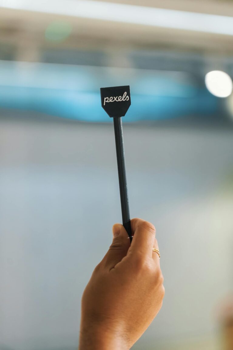 A hand holding a small sign with 'pexels' text, blurred background.