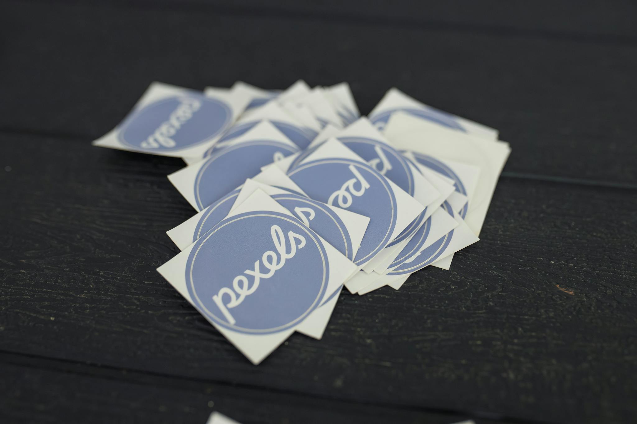 A pile of Pexels logo stickers arranged on a dark wooden surface.
